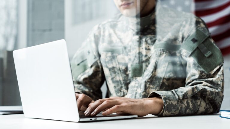 cropped view of soldier in camouflage uniform using laptop