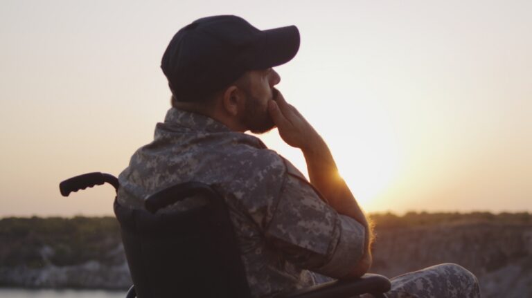 veteran is sitting sitting in the wheelchair on a meadow at sunset