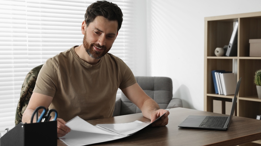 Happy soldier working with documents at wooden table indoors. Military service