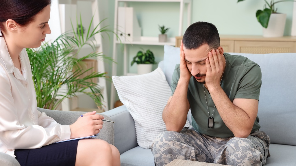 Sad young soldier with PTSD and psychologist sitting in office