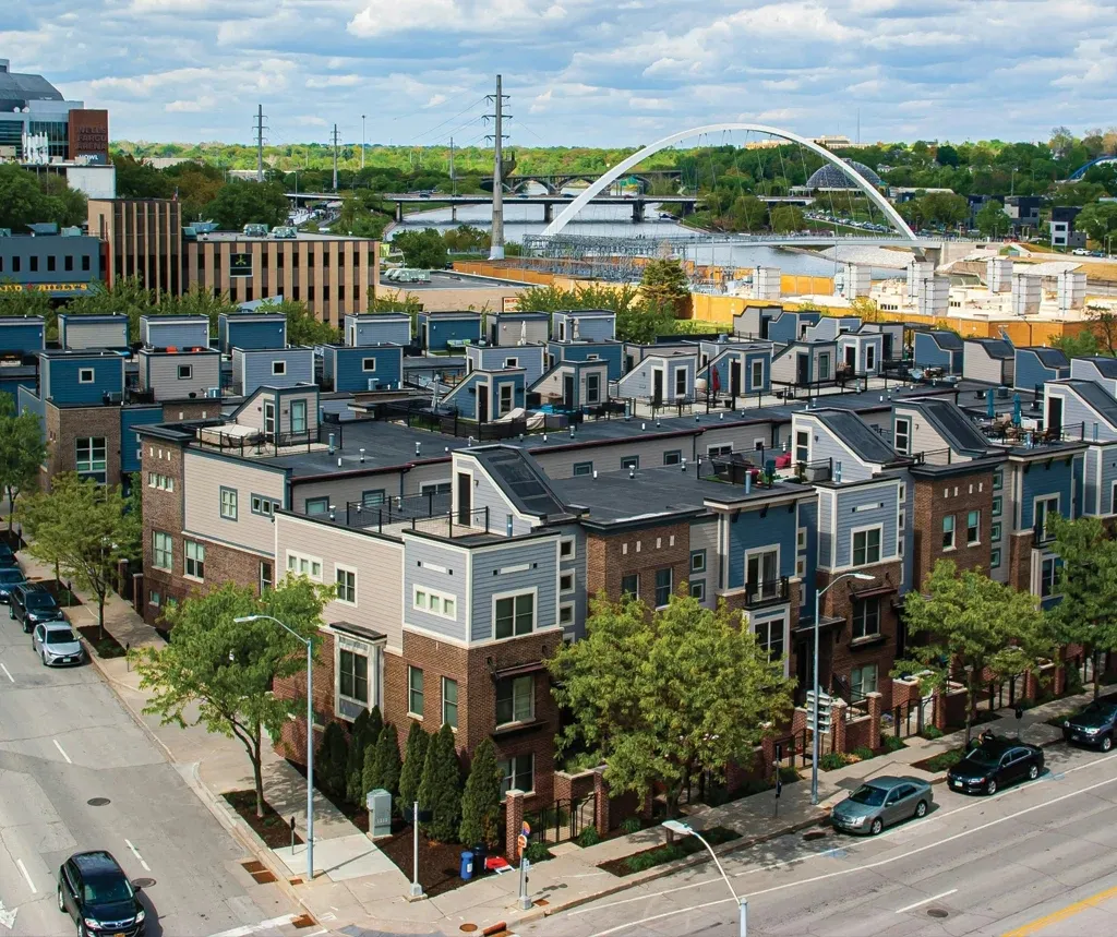 Aerial view of modern townhouses with rooftop patios near a river and white arched bridge.